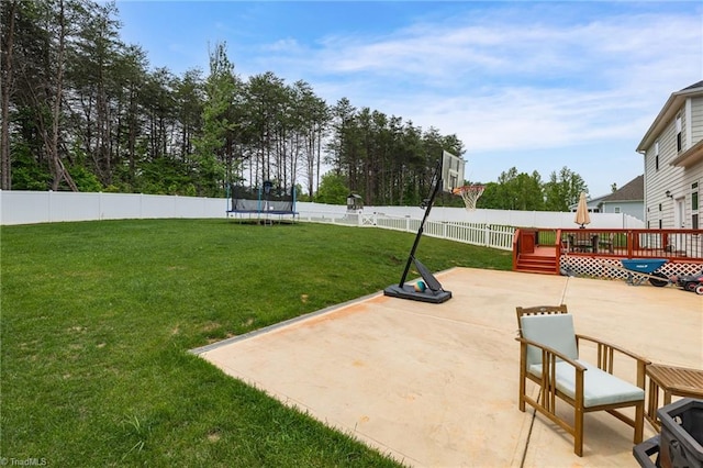 exterior space with a trampoline, a yard, a wooden deck, and a patio area