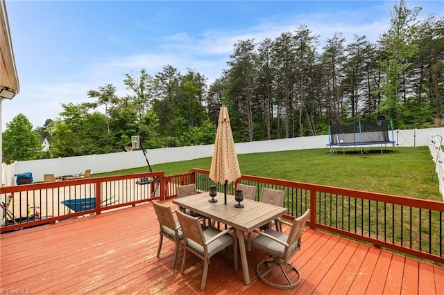 wooden deck with outdoor dining area, a yard, a fenced backyard, and a trampoline
