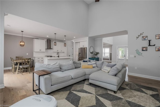 living room featuring a towering ceiling, light wood-type flooring, crown molding, and sink