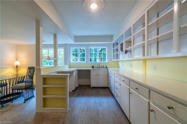 kitchen with sink, kitchen peninsula, hardwood / wood-style floors, and white cabinets