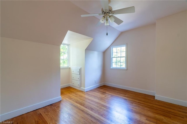 additional living space with vaulted ceiling, a healthy amount of sunlight, ceiling fan, and light hardwood / wood-style flooring