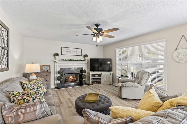 living room with a high end fireplace, a textured ceiling, light hardwood / wood-style floors, and ceiling fan