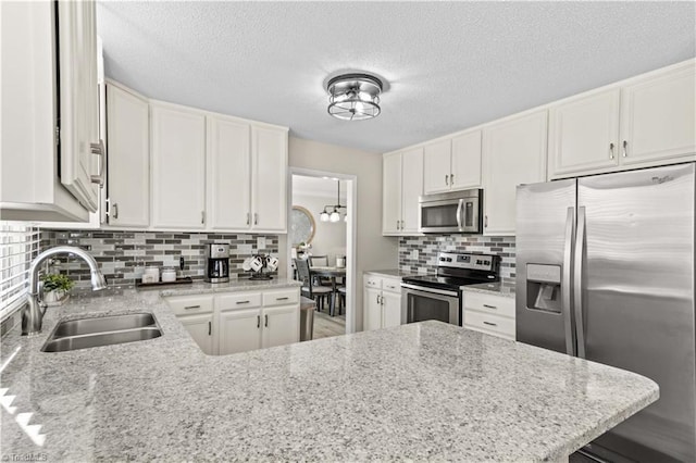 kitchen with white cabinets, stainless steel appliances, light stone countertops, and sink