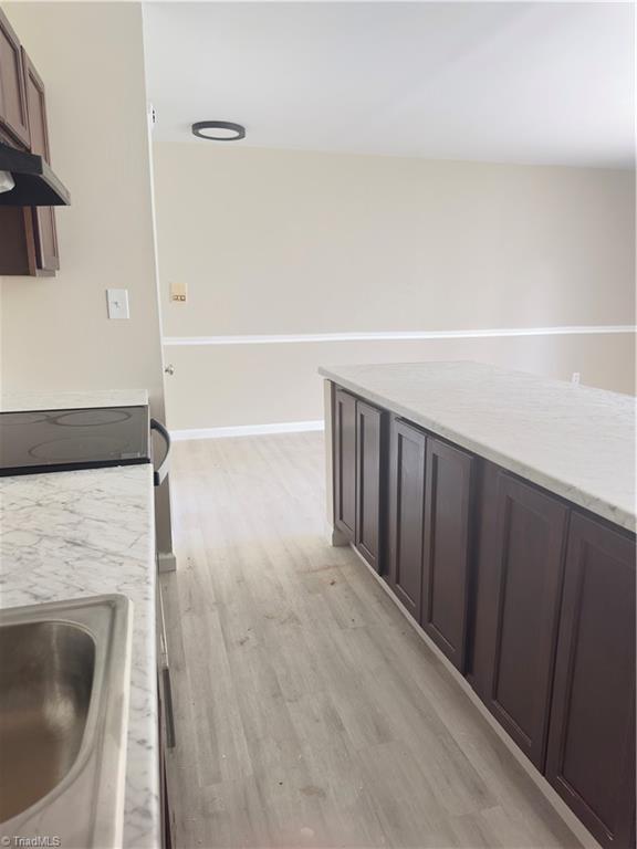 3109 Darden Rd Unit B, Greensboro, NC 27407 - kitchen with under cabinet range hood, light wood-style flooring, stove, and dark brown cabinets