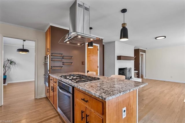 kitchen with light wood-style floors, appliances with stainless steel finishes, island range hood, crown molding, and a brick fireplace