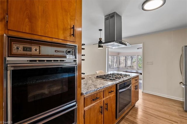 kitchen with a warming drawer, light wood-type flooring, island exhaust hood, stainless steel appliances, and brown cabinetry