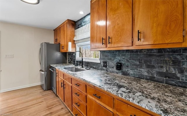 kitchen featuring brown cabinets, stone countertops, a sink, dishwasher, and light wood-type flooring