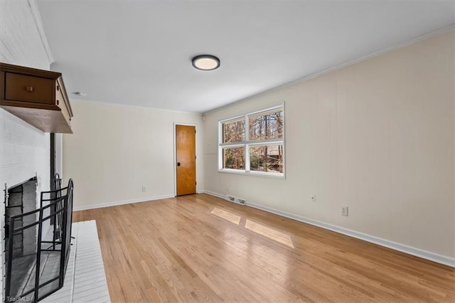 unfurnished living room featuring visible vents, baseboards, light wood finished floors, crown molding, and a brick fireplace