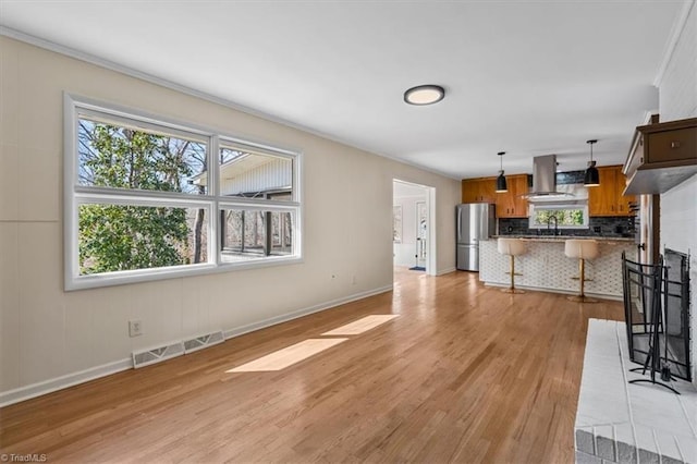 unfurnished living room with a sink, visible vents, baseboards, and light wood-style flooring