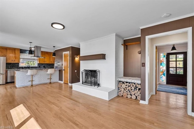 living area featuring baseboards, a fireplace, light wood-style flooring, and crown molding