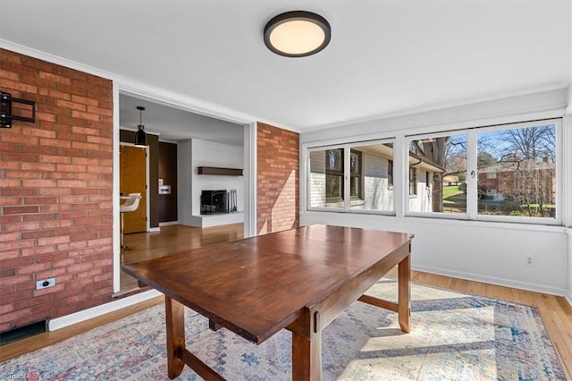 unfurnished dining area featuring brick wall, crown molding, baseboards, a fireplace, and wood finished floors