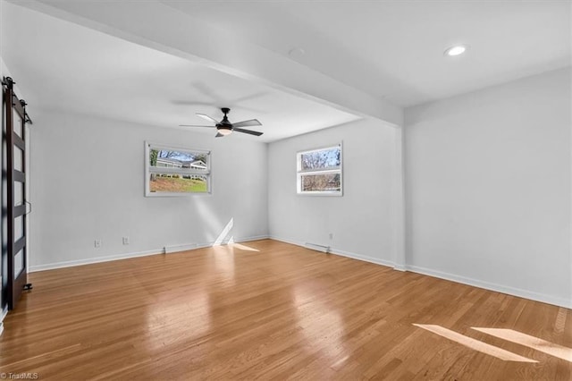 spare room featuring a ceiling fan, a barn door, wood finished floors, and baseboards