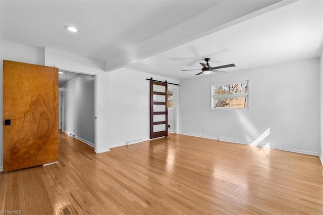 empty room featuring light wood-type flooring, beam ceiling, a ceiling fan, a barn door, and baseboards