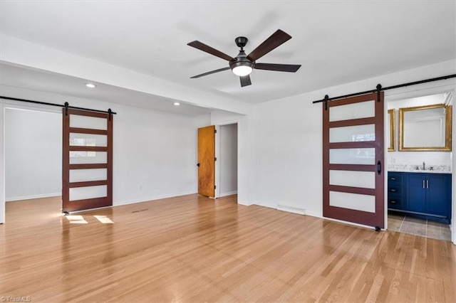 spare room featuring a sink, a barn door, light wood-style flooring, and a ceiling fan