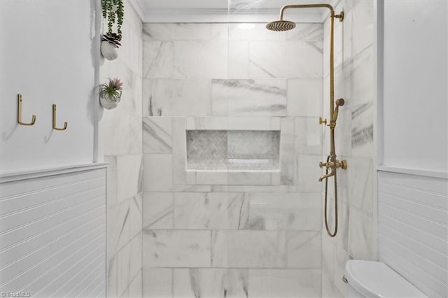 bathroom featuring a wainscoted wall, tiled shower, toilet, and tile walls