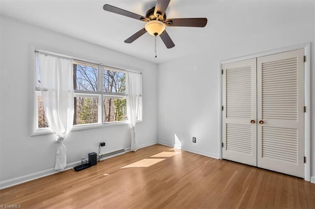 unfurnished bedroom featuring a closet, baseboards, wood finished floors, and a baseboard heating unit