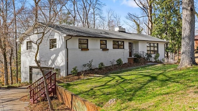 view of front of home featuring a front yard, driveway, an attached garage, a chimney, and brick siding