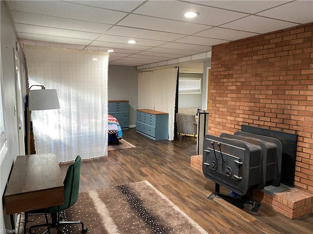 bedroom featuring brick wall, a wood stove, a paneled ceiling, and wood finished floors