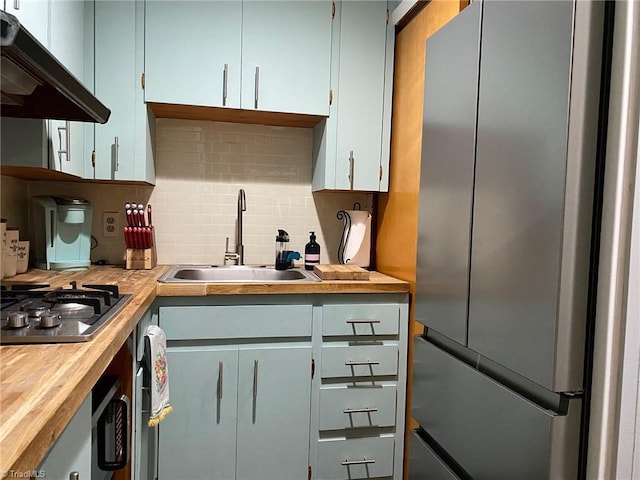 kitchen with under cabinet range hood, backsplash, appliances with stainless steel finishes, and a sink