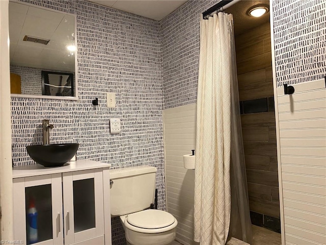 bathroom with tiled shower, toilet, tile walls, and vanity