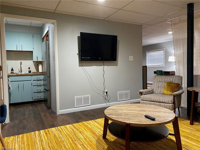 living room featuring dark wood-style floors, visible vents, baseboards, and a drop ceiling