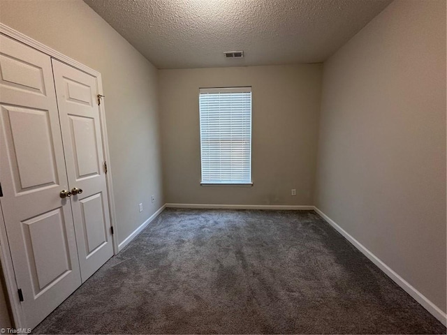 unfurnished room featuring a textured ceiling and dark colored carpet