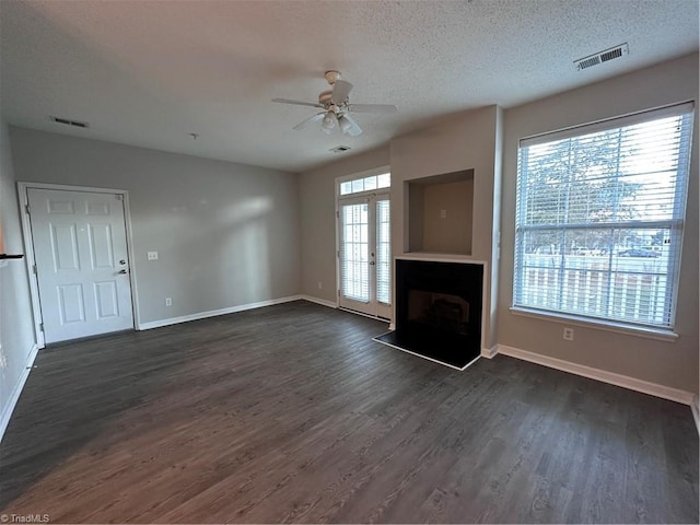 unfurnished living room featuring ceiling fan, plenty of natural light, a textured ceiling, and dark hardwood / wood-style flooring