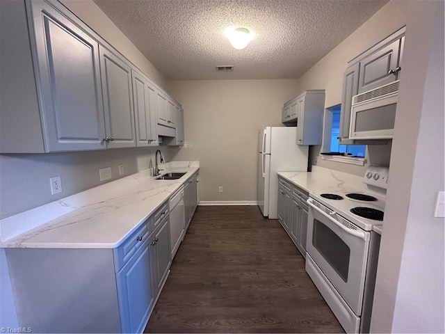 kitchen featuring sink, white appliances, light stone countertops, dark wood-type flooring, and a textured ceiling