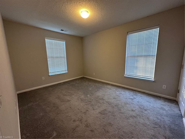 empty room with a textured ceiling and dark colored carpet