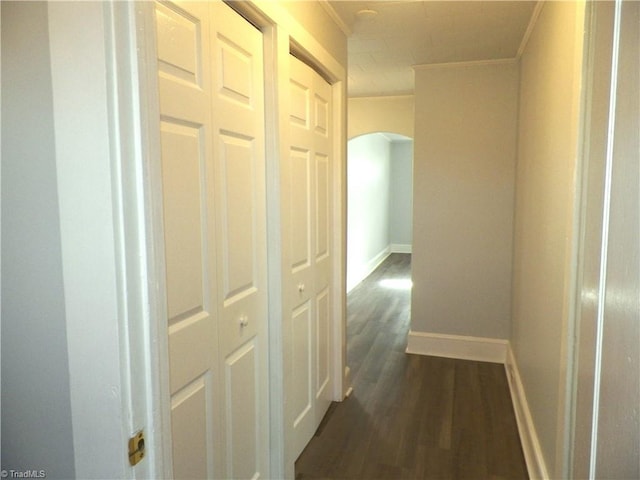 hall with baseboards, arched walkways, dark wood-type flooring, and crown molding