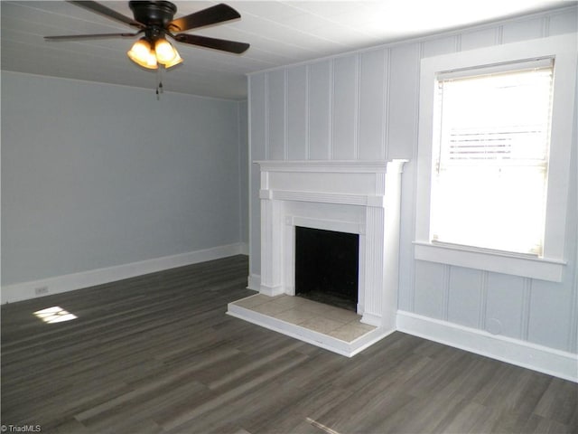 unfurnished living room with a tile fireplace, dark wood finished floors, baseboards, and ceiling fan