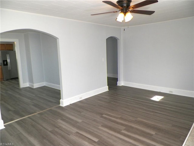 empty room with dark wood-style floors, arched walkways, crown molding, a ceiling fan, and baseboards