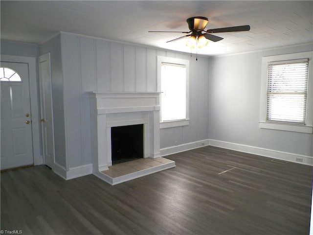 unfurnished living room with ornamental molding, dark wood-type flooring, a tiled fireplace, and baseboards