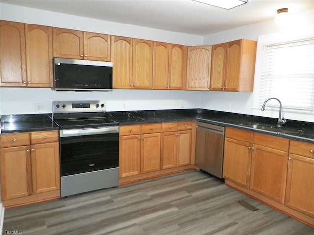 kitchen with brown cabinets, visible vents, appliances with stainless steel finishes, light wood-style floors, and a sink