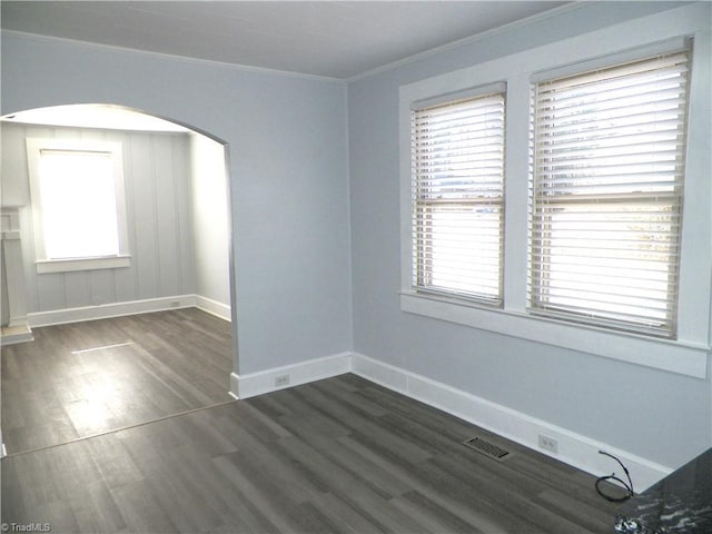 unfurnished room with arched walkways, visible vents, ornamental molding, wood finished floors, and baseboards