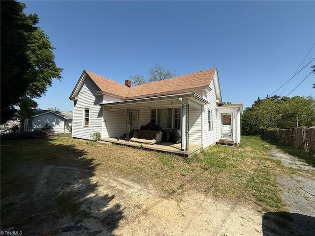 back of house featuring fence, a porch, a chimney, and a shingled roof