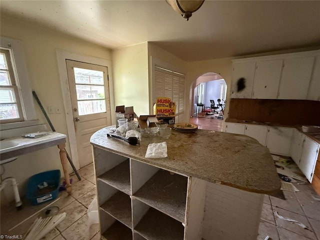 kitchen with arched walkways, plenty of natural light, white cabinetry, and light countertops