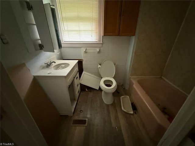 full bath with toilet, vanity, wood finished floors, and tile walls
