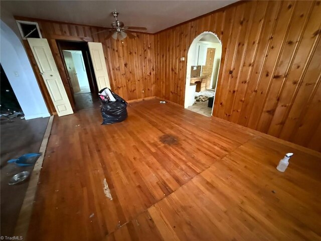 unfurnished dining area featuring arched walkways, wood finished floors, ceiling fan, wooden walls, and baseboards