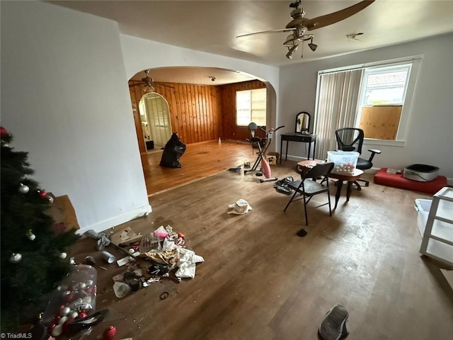 living area with arched walkways, wood finished floors, a ceiling fan, and baseboards