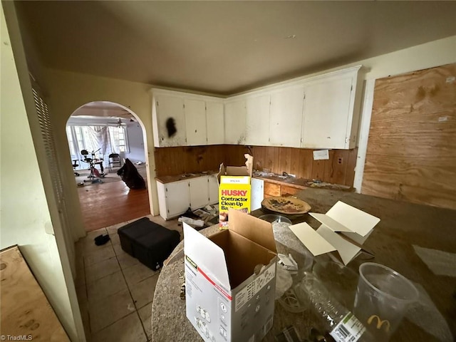 kitchen with arched walkways, white cabinets, light tile patterned floors, and wood walls