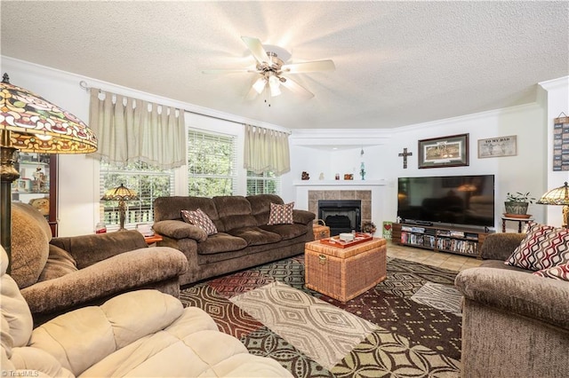 living room featuring ornamental molding, a textured ceiling, ceiling fan, and a tile fireplace