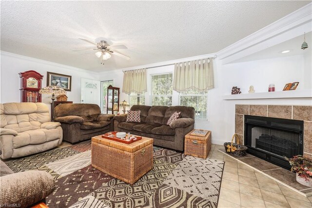 tiled living room with a ceiling fan, a textured ceiling, ornamental molding, and a tiled fireplace