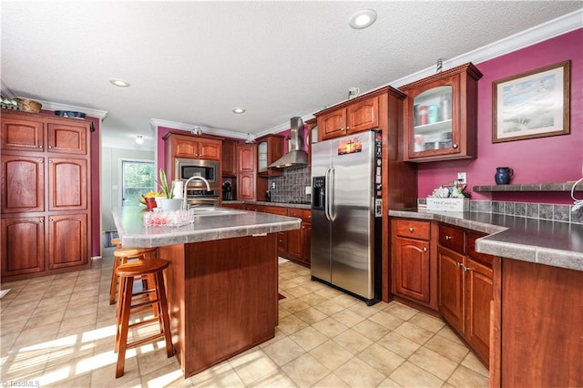 kitchen with glass insert cabinets, a breakfast bar area, wall chimney range hood, a sink, and stainless steel appliances