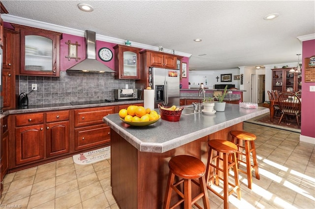kitchen featuring wall chimney range hood, a sink, stainless steel fridge, and light tile patterned floors