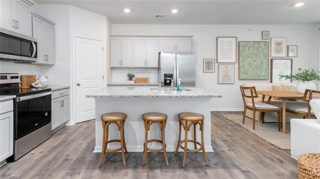 kitchen with light stone counters, stainless steel appliances, and a center island with sink