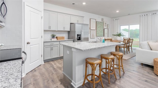 kitchen featuring sink, light stone counters, light hardwood / wood-style floors, an island with sink, and stainless steel fridge with ice dispenser