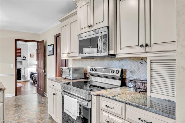 kitchen with light stone counters, decorative backsplash, a fireplace, appliances with stainless steel finishes, and ornamental molding