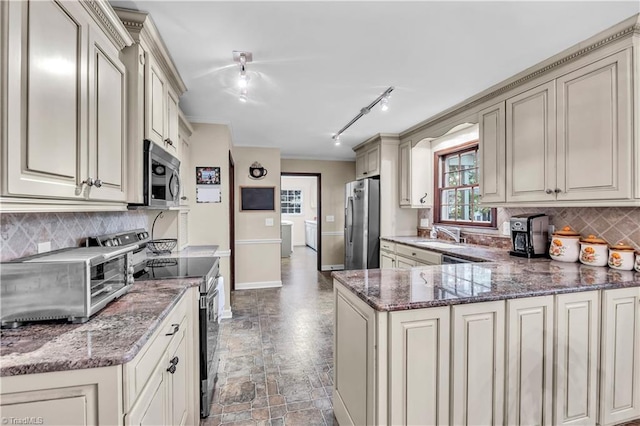 kitchen with kitchen peninsula, appliances with stainless steel finishes, decorative backsplash, track lighting, and dark stone countertops