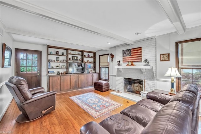 living room featuring beam ceiling, light hardwood / wood-style floors, and a brick fireplace